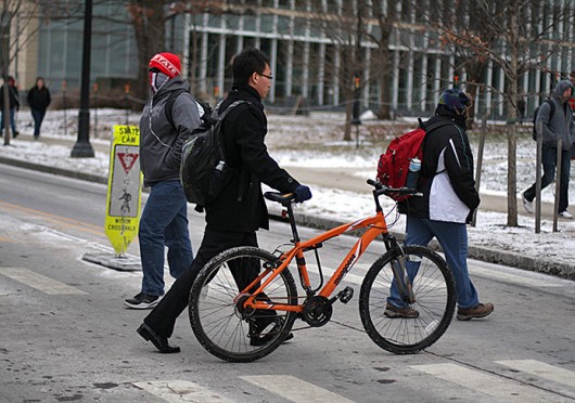 A man walks a bike across 18th Avenue. OSU students living on 4th and Summit streets could soon see designated biking lanes on their roads. Credit: Shelby Lum / Photo editor