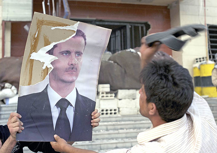 A fighter beats a poster of Syrian President Bashar al-Assad after rebel forces stormed a government position in Al-Tall, Syria, July 19, 2012.