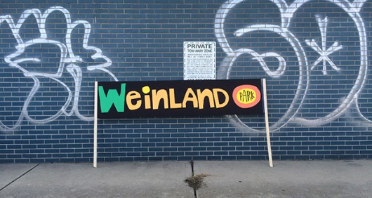 A sign, which supporters carried to the new mural's unveiling, leans against a graffitied building. Credit: Nick Roll / Lantern Reporter